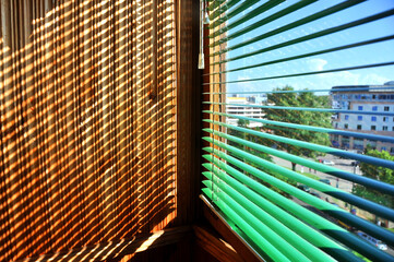 Sunlight through wooden and green blinds on a balcony with city view