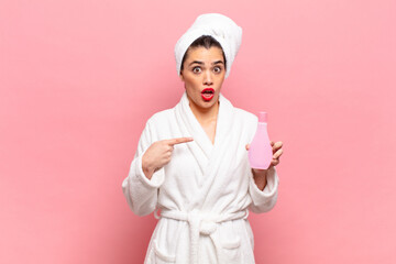 young pretty woman looking shocked and surprised with mouth wide open, pointing to self. bathrobe...