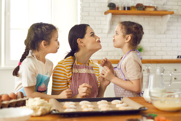 Family cooking together in the kitchen. Playful mom and daughters make cookies and have fun making mustaches out of dough. Concept of spending time together mother and child, motherhood and childhood.
