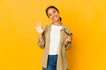 Young hispanic woman holding a smoking pipe smiling cheerful showing number five with fingers.