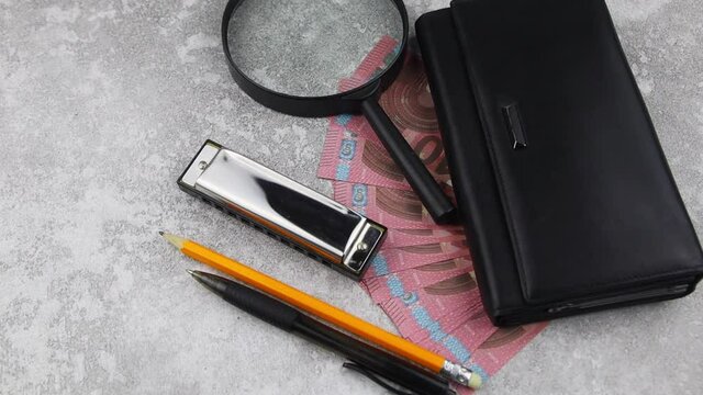 Financial, business success or analysis concept with 10 Euro bills fanned below a purse with magnifying glass, pen and pencil on a decorative wood background in a high angle view. Rotating table