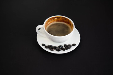 White cup of aromatic freshly ground arabica coffee on a black background. The cup is on the saucer. White cup of aromatic freshly ground arabica coffee on a black background. Top view.