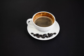 White cup of aromatic freshly ground arabica coffee on a black background. The cup is on the saucer. White cup of aromatic freshly ground arabica coffee on a black background. Top view.
