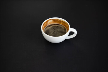 White cup of aromatic freshly ground arabica coffee on a black background. The cup is on the saucer. White cup of aromatic freshly ground arabica coffee on a black background. Top view.