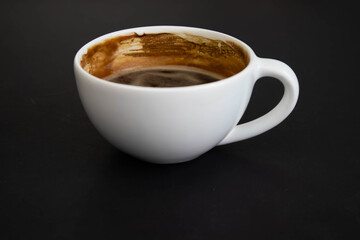 White cup of aromatic freshly ground arabica coffee on a black background. The cup is on the saucer. White cup of aromatic freshly ground arabica coffee on a black background. Top view.