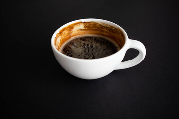 White cup of aromatic freshly ground arabica coffee on a black background. The cup is on the saucer. White cup of aromatic freshly ground arabica coffee on a black background. Top view.