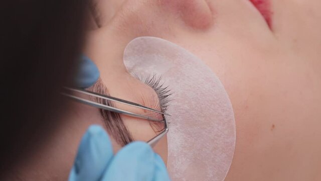 Eyelash extension procedure. The working process of professional beauty master lengthening female lashes. Fake eyelashes. Eyelashes extensions close up. Makeup artist and client in beauty salon