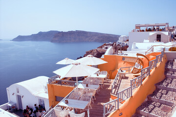 Santorini, Greece - September 11, 2017: Cyclades architecture hotels houses and cafes over the caldera in Oia santorini greek islands against mediterranean sea view with mountains - obrazy, fototapety, plakaty