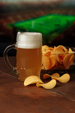 Glass of cold beer and snack in front of screen with football game. Vertical image.