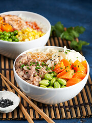Two assorted poke bowls, pulled pork, vegetables, pumkin, soy beans edamame, noodles, on bowl, chopsticks. blue dark background. Closeup. Trendy asian food. Healthy, clean eating concept.