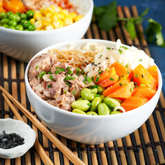 Two assorted poke bowls, pulled pork, vegetables, pumkin, soy beans edamame, noodles, on bowl, chopsticks. blue dark background. Closeup. Trendy asian food. Healthy, clean eating concept.