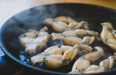 Traditional cooking of fried frog legs on pan.