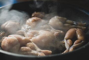 Traditional cooking of fried frog legs on pan.