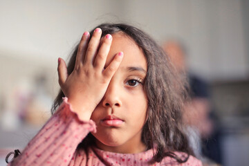 little girl covers one eye with her hand