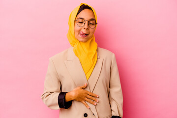 Young business muslim woman isolated on pink background touches tummy, smiles gently, eating and satisfaction concept.