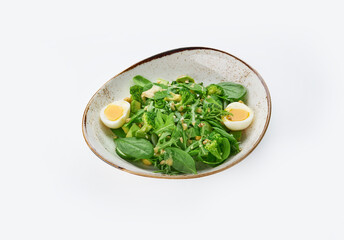 Tasty green healthy salad with spinach leaves, avocado and boiled eggs in bowl on white background