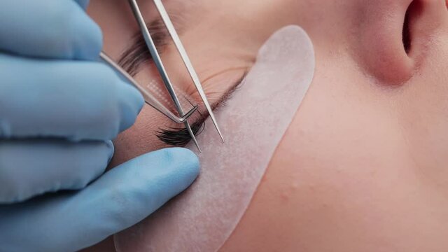 Eyelash extension procedure. The working process of professional beauty master lengthening female lashes. Fake eyelashes. Eyelashes extensions close up. Makeup artist and client in beauty salon.
