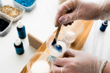 artist stirring blue dye in a plastic cup with epoxy resin - obrazy, fototapety, plakaty