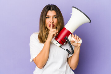 Young indian woman holding a megaphone isolated keeping a secret or asking for silence.