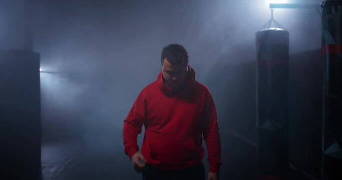 Portrait, boxer takes off the hood from his head, serious expression before the fight. Dark gym with smoke, preparation for the fight. 4k, ProRes