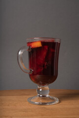 A glass of red wine mulled wine with apples and oranges is on a wooden table.