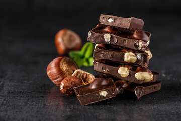 Stack of chocolate slices with mint leaf.Hazelnut and almond milk and dark chocolate pieces tower.Sweet food photo concept. The chunks of broken chocolate