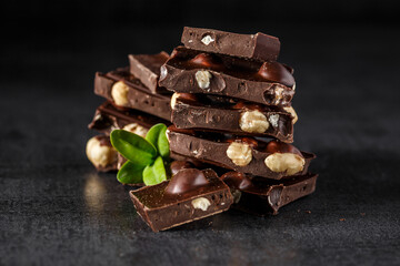 Stack of chocolate slices with mint leaf.Hazelnut and almond milk and dark chocolate pieces tower.Sweet food photo concept. The chunks of broken chocolate