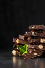 Stack of chocolate slices with mint leaf.Hazelnut and almond milk and dark chocolate pieces tower.Sweet food photo concept. The chunks of broken chocolate