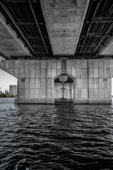 View through the pillars of the bridge. The left bank of the Dnieper in the city of Kiev. Under the bridge. Black and white photo