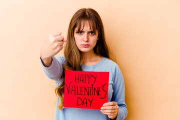 Fototapeta na wymiar Young caucasian woman holding a Happy Valentines day isolated showing fist to camera, aggressive facial expression.