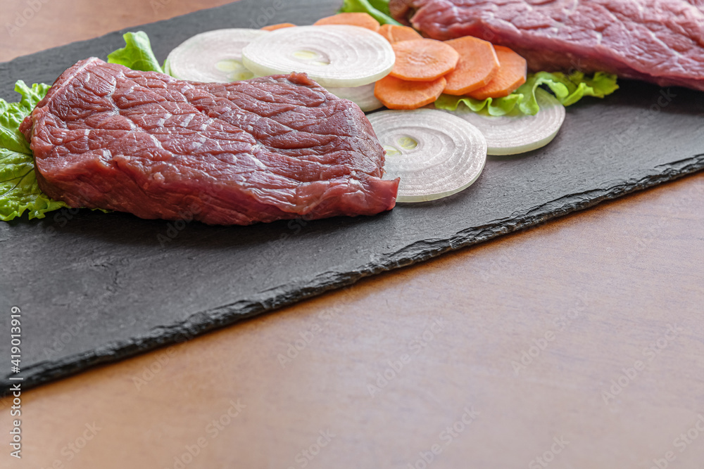 Wall mural fresh raw meat with carrot and onion slices a black slate surface