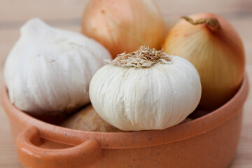 A lot of vegetables. Red onions. garlic and potato in a yellow pot. Wooden table background