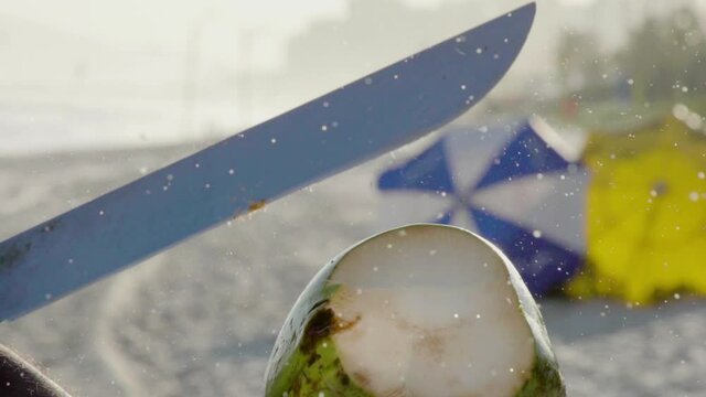 Close-up of opening coconut with machete at beach, slow motion.