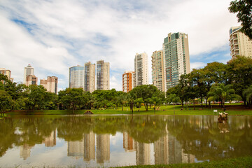Fototapeta na wymiar Lago no Parque Flamboyant, com prédios e céu com nuvens ao fundo em dias de lockdown.