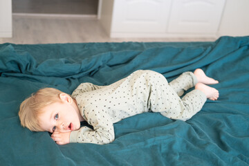 Little healthy toddler boy in green pajamas having fun lying in bed at home