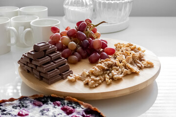 Red grapes, walnuts, chocolates and pie lie on a white table. High quality photo