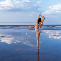sexy girl in white on the mirror surface of the salt lake. flexible gymnast performs split among the clouds