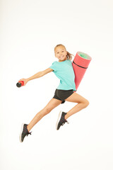 Cheerful girl with yoga mat and bottle of water jumping in studio