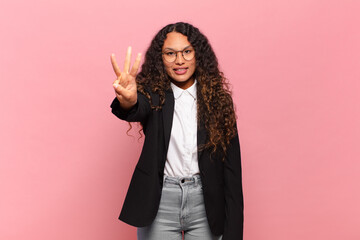 young hispanic woman smiling and looking friendly, showing number three or third with hand forward,...