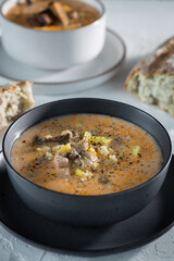 Cream cheese soup with mushrooms and potatoes, delicious first course in black bowl on the white table, vertical
