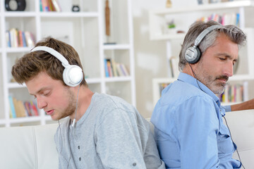 Man and adolescent back to back wearing headphones