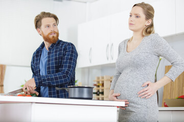 husband and pregnant woman with ache standing in the kitchen