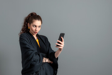 Fototapeta premium curly-haired emotional teenager woman in a black cloak talking by video call on smartphone