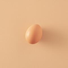 Single natural egg standing on a pastel beige paper background. 2021 Easter unique still life layout. Minimal retro creative idea.