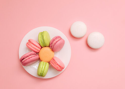 Macaroons Cute flat lay photo for posters and banners Multicolored macarons on white small plate and two white almond biscuits on pink background