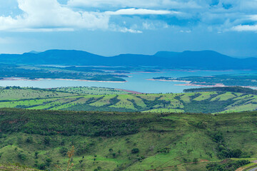 Wide panoramic view of nature beauties of Minas Gerais state on a cloudy day. Vast green area with a mountainous terrain and the Lake of Furnas on background. Capitólio MG, Brazil. 