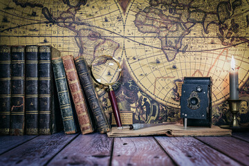 still life composed of antique books, camera and clock on a background of a classic map.