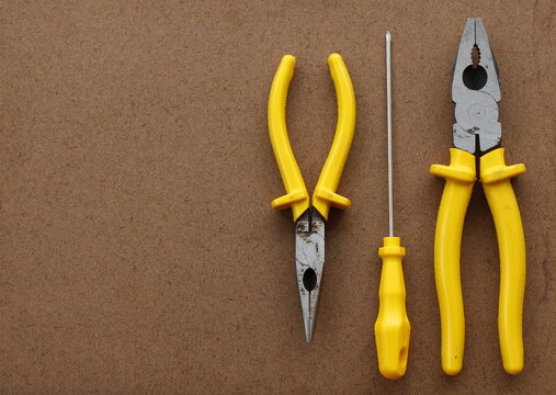 yellows hand tools for home use (two pliers and a screwdriver) on a plywood texture.