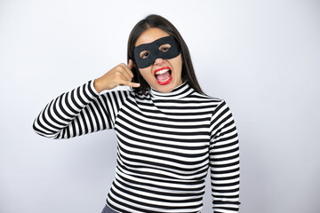 Young beautiful brunette burglar woman wearing mask smiling doing phone gesture with hand and fingers like talking on the telephone
