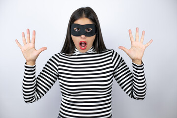Young beautiful brunette burglar woman wearing mask showing and pointing up with fingers number ten smiling confident and happy